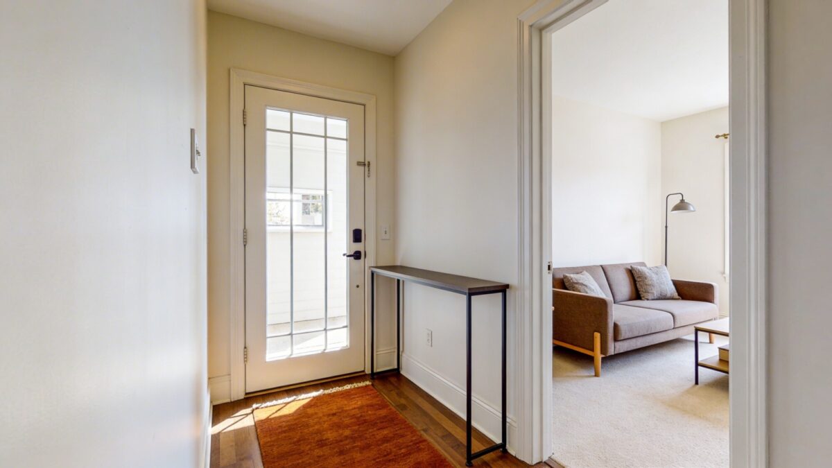 A small entryway opening directly into a cozy living room, with a slim console table by the door, a warmly colored rug signaling the welcome path, and a compact sofa placed diagonally to avoid blocking the doorway, in natural daylight.