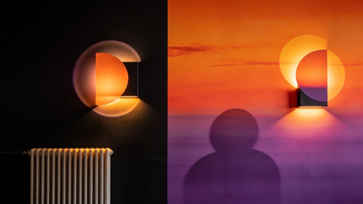 Dramatic sunset-inspired wall design: lamp art wallpaper with strong orange-to-purple gradients, soft halos around abstract forms, a black accent wall, and a minimalist radiator decor with warm lighting.