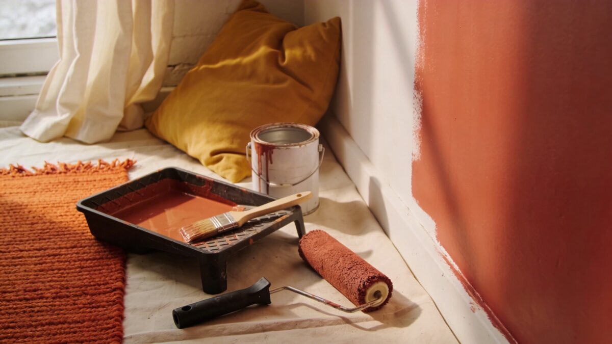 A DIY-friendly mood in-progress shot: painting one wall a bold color, painting supplies neatly arranged, and textiles chosen to coordinate, illustrating budget-friendly makeover steps.