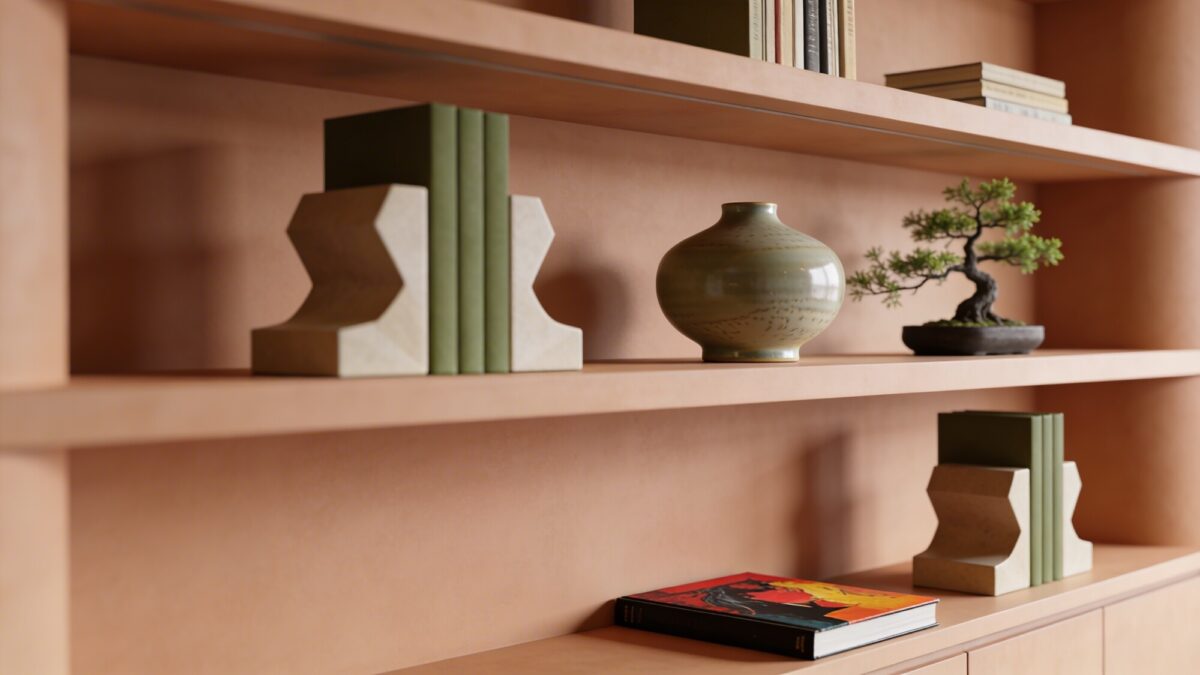 A minimal, curated bookshelf display focused on earth tones, including sculptural bookends, a matte-glazed ceramic piece, a small bonsai or succulent, and a single bold art book lying flat, shot from a slightly elevated angle.